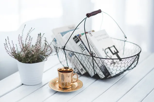 Una canasta de libros y una taza de café con una maceta de plantas al costado descargar