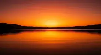 e brillanten orange sonnenennergang werft schimmernd reflexiounen op engem rouegen sei, mat waiten silhouetten vun hiwwelen, dei den friddlechen horizont saumen. eroflueden