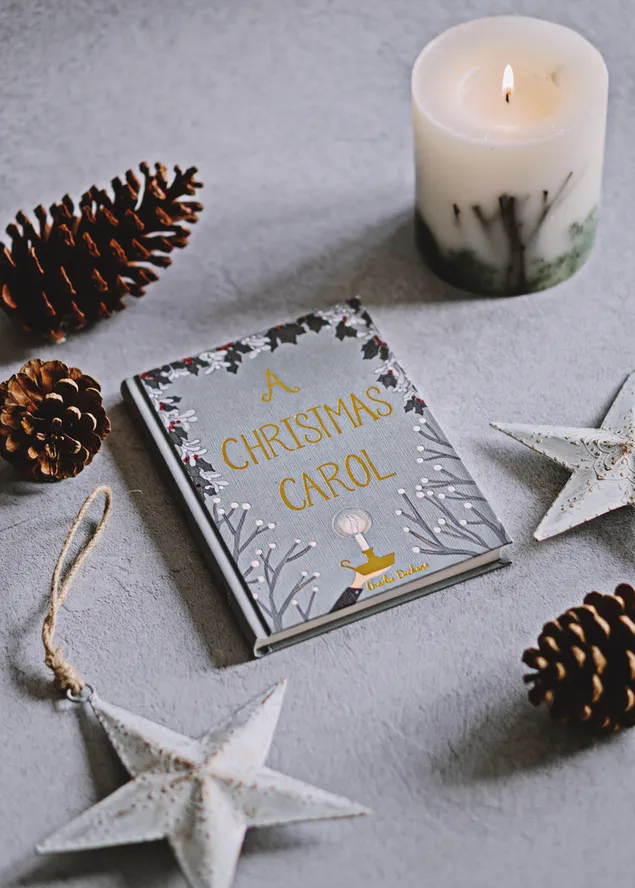 A Christmas Carol story book with candles, pinecones and star decor