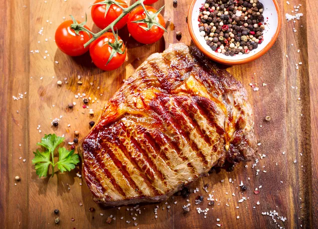 נתח סטייק טעים מתבל במלח ופלפל שחור עם עגבניות במגש עץ 4K טפט