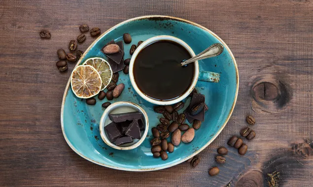 Secangkir kopi hitam dan lemon kering, biji kopi di piring keramik biru