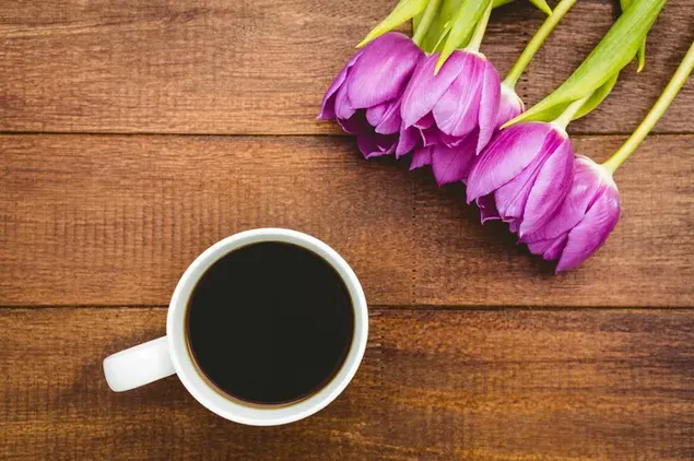 Secangkir kopi hitam dan tulip ungu di meja kayu