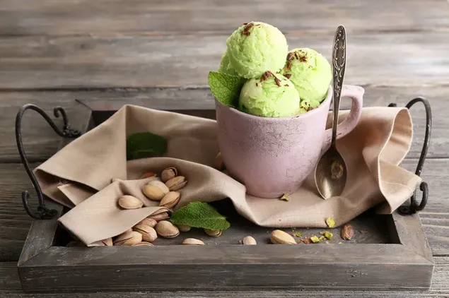 Una taza de helado verde con sabor a pistacho en una bandeja colocada en una mesa de madera 4K fondo de pantalla