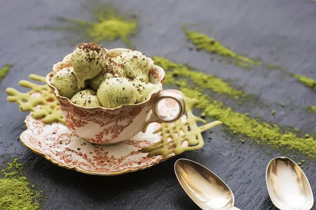 Secangkir es krim matcha yang lezat dengan taburan bubuk matcha di sampingnya
