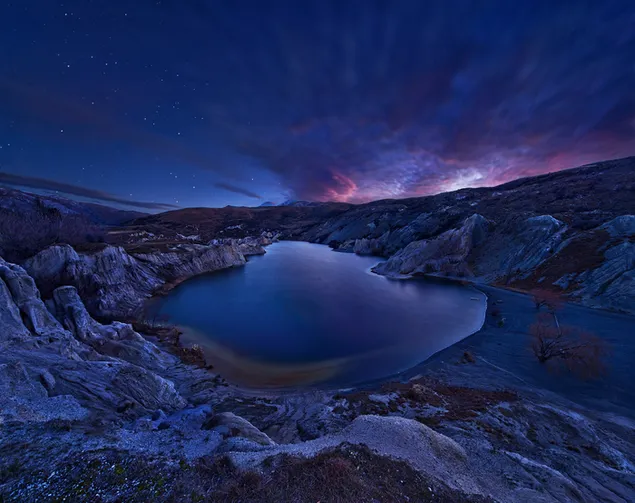 Un lago magnífico entre los acantilados entre las luces de las nubes en la noche