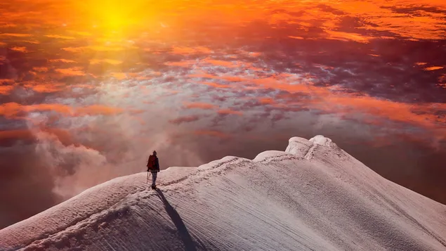 Преземете Човек кој стои на снежна планинска карпа и го гледа зајдисонцето