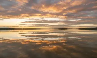 a tranquil lake mirrors the glowing golden clouds at sunset, creating a peaceful and atmospheric landscape filled with warm natural beauty download