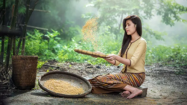 A woman in a yellow dress with black long hair is busy with wheat in a  yellow wicker basket in the oxygen-rich forest 4K wallpaper download