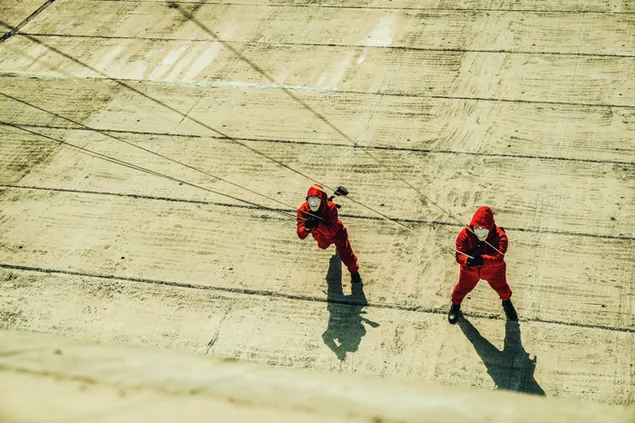 Aktoriai raudonomis suknelėmis, lipantys ant medinių grindų filme „Money Heist Korea Joint Economic Area“. 2K ekrano užsklanda