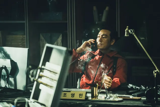 Aktorė raudona suknele, rūkanti cigaretę, sėdi prie stalo filme „Money Heist Korea Joint Economic Area“. HD ekrano užsklanda
