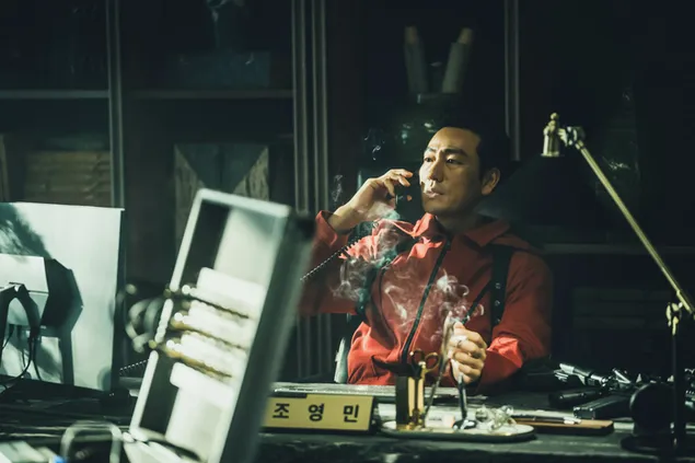Actriz vestida de rojo fumando cigarrillos sentada en un escritorio en la película Money Heist Korea Joint Economic Area