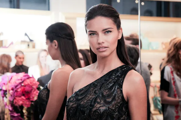 Taustakuva Adriana Lima mustassa asussa vaaleanpunaisten kukkien vieressä 2K