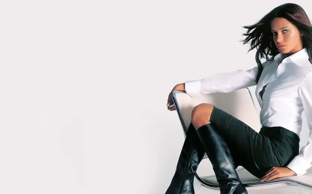Taustakuva Adriana Lima valkoisessa paidassa, vihreässä lyhyessä housussa, jossa mustat saappaat istuu valkoisella tuolilla, valkoisella taustalla HD