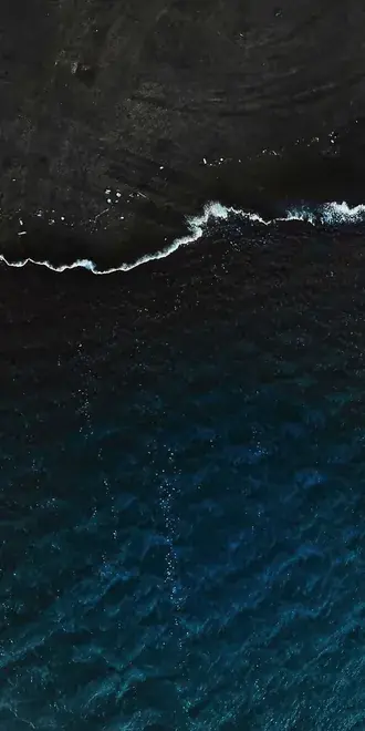aerial top down view of dark ocean waves crashing on rocky black coastline download