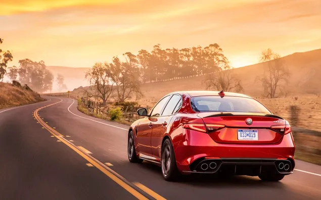 Alfa Romeo op asfaltweg bij zonsondergang download