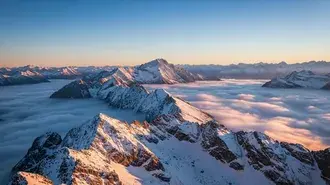 alpesi hajnal a felhok felett, havas csucsokkal, amelyek lagy reggeli fenyben es vegtelen egbolton emelkednek ki letoltes