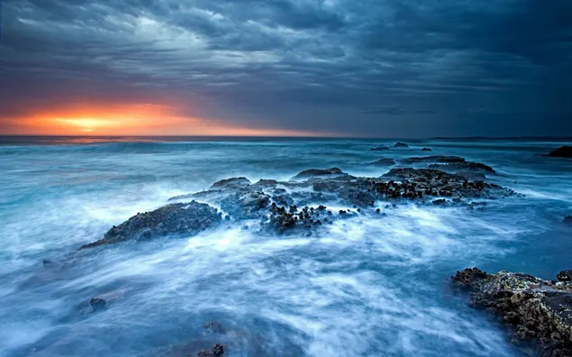 暗い曇り空に夕日と海の波を設定する間の石