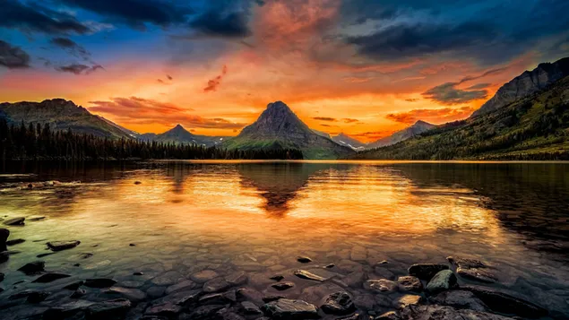 暗い雲と赤い日の出の光を反射する湖の周りの山と石
