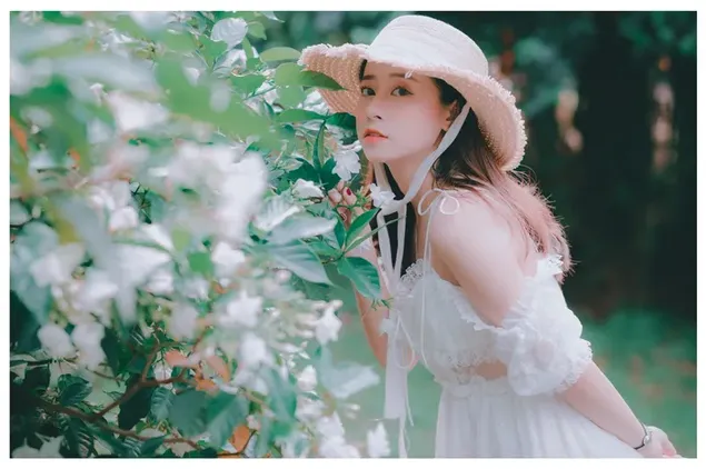 花の植物のそばに白いドレスと麦わら帽子をかぶったアジアの女の子