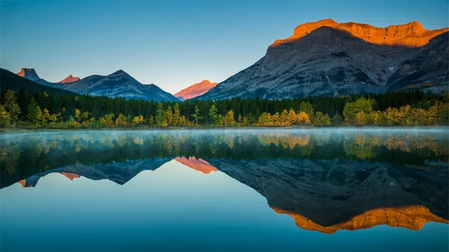 丘の頂上、太陽の黄色い光と木々や岩が湖に映る