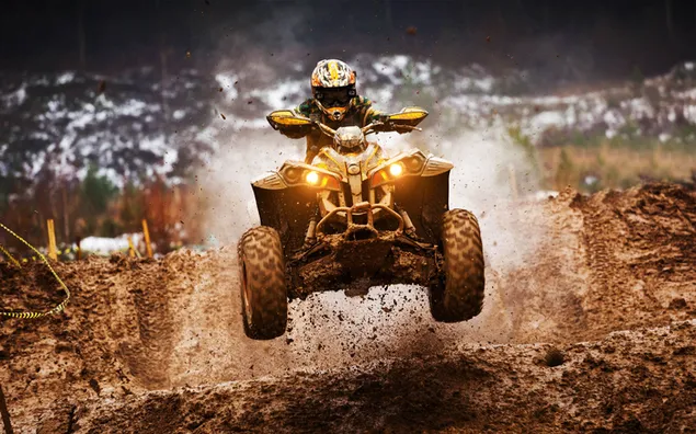 雪に覆われた背景をぼかした写真の前に泥だらけの未舗装の道路を走行する Atv