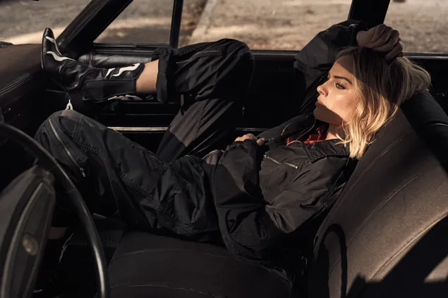 Australian Margot Robbie in black track suit and black boots inside a car