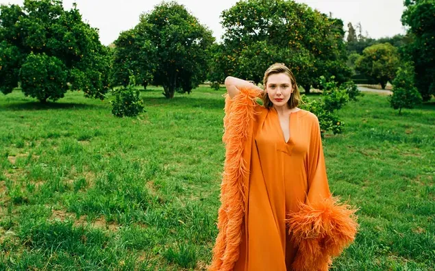 Die schöne Schauspielerin Elizabeth Olsen trägt ein orangefarbenes langes Kleid mit grünem Naturhintergrund