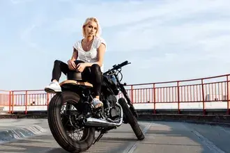 Tapeta Krásná blondýnka na černém motocyklu na asfaltové silnici obklopené červenými strážemi s výhledem na oblohu 4K