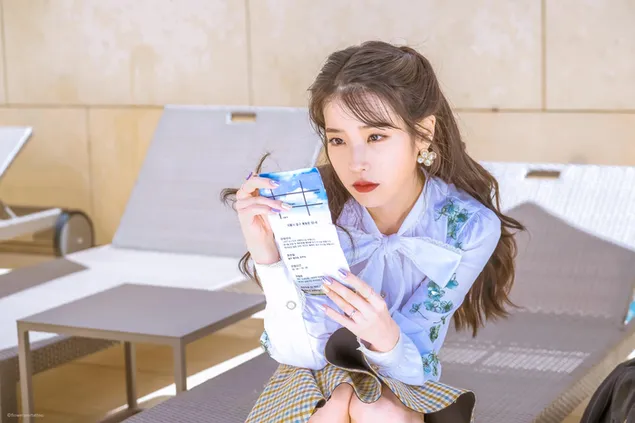 הזמרת היפה IU קוראת משהו בצל על שזלונג, לובשת בגד כחול לבן עם שיער חום ארוך 4K טפט