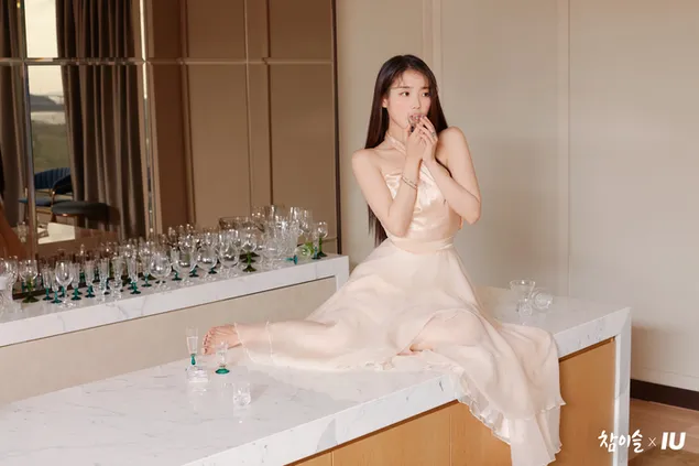 Schöne Sängerin IU posiert zu Hause auf Marmor in einem hellrosa Outfit, langen braunen Haaren und hält ihre Hand vor ihr Gesicht 6K Hintergrundbild