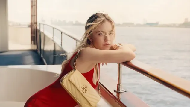La hermosa Sydney Sweeney luciendo un sexy vestido rojo con un bolso de hombro de diseñador en un barco