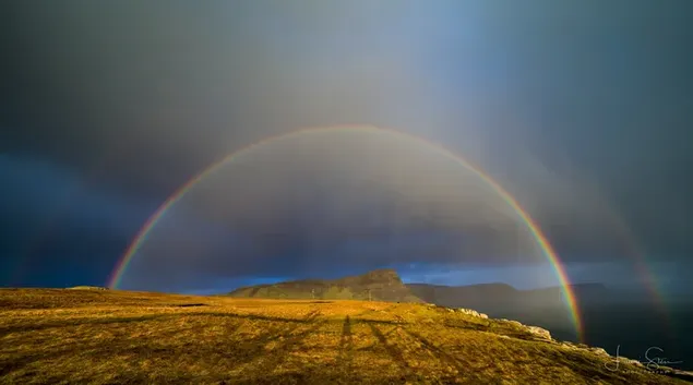 Más allá del campo plano, la majestuosa vista del arcoíris formado bajo la lluvia se ve impresionante. descargar