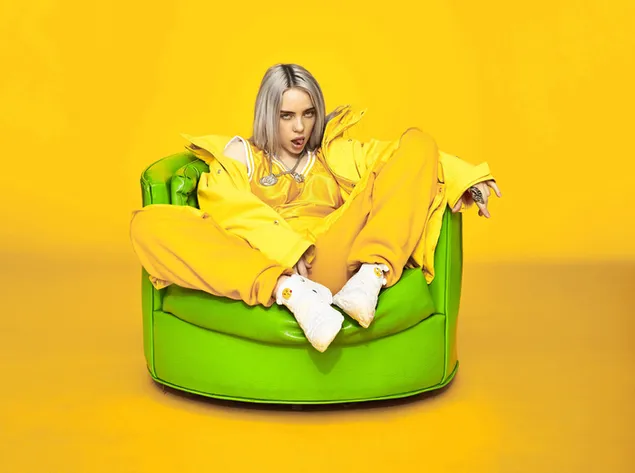Billie Eilish draagt ​​een geheel gele outfit zittend op een groene bank