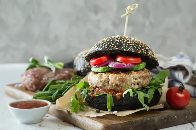 Hamburguesa negra con hamburguesa gruesa de ternera, tomates y pepino con ketchup al lado 4K fondo de pantalla