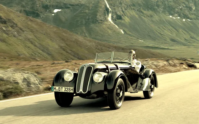 Mobil sport vintage hitam terbuka atas mengemudi di jalan tanah di sebelah bukit bersalju