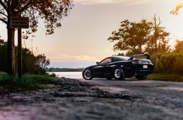 Schwarzer Toyota Supra bei Sonnenuntergang, zwischen den Bäumen 4K Hintergrundbild