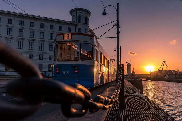 Blau-weißer Zug, der bei Sonnenuntergang am Meer in der Stadt fährt