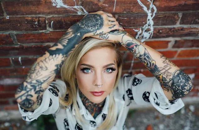 Blonde girl with blue eyes and tattoos in a brick wall background