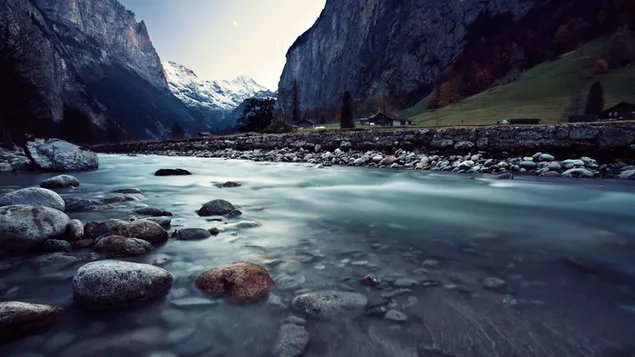 Vista mozzafiato dell'acqua che scorre tra colline e alte montagne innevate che sembrano vicine al cielo 4K sfondo