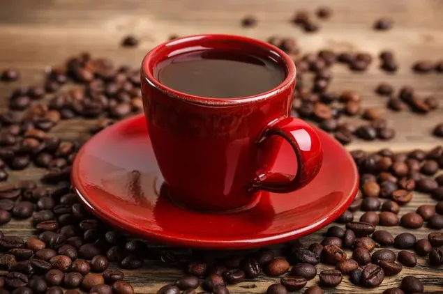 Café clásico en una taza roja vibrante con granos de café esparcidos en la mesa