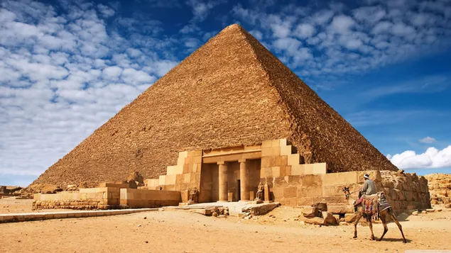 Camello y humano en la arena del desierto frente al cielo nublado y las pirámides egipcias