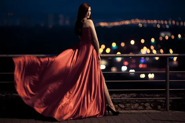 Mujer de pelo largo castaño con vestido largo con vistas borrosas a las luces de la ciudad 2K fondo de pantalla