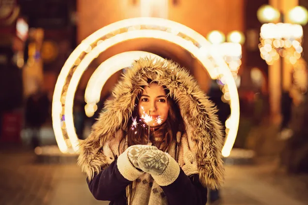 Chica guapa sosteniendo un petardo Sparkler con fondo borroso de luces de Navidad