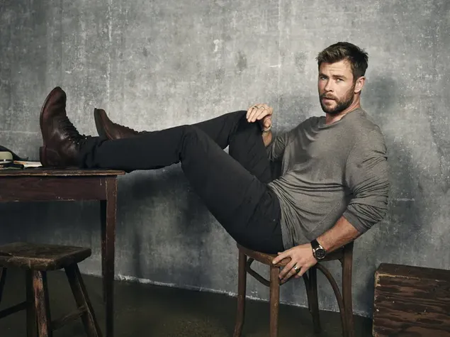 chris hemsworth dengan celana hitam dan sepatu bot coklat duduk di atas meja kayu di dalam ruangan dengan sepatunya unduhan