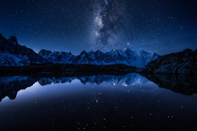 Cielo, estrellas y montañas nevadas reflejadas en el lago al atardecer