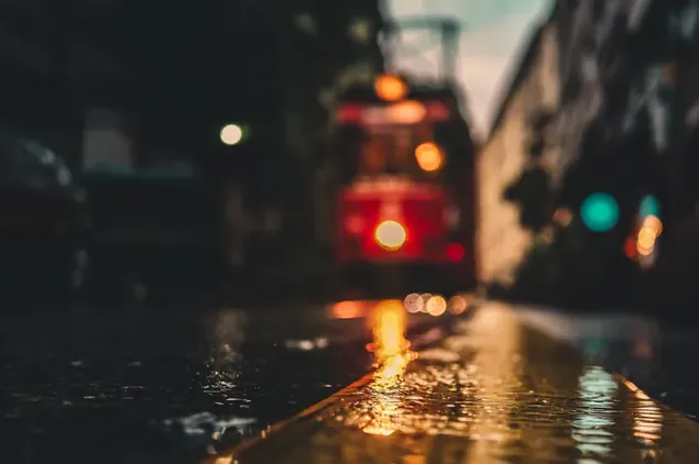 Lampu kota terpantul di air dalam cuaca hujan di jalan pada malam hari dan kereta merah bergerak di rel unduhan