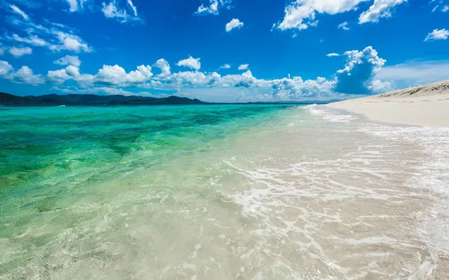 Heldergroen water dat het strand raakt en witte wolken in de lucht met een echte blauwe kleur 4K achtergrond