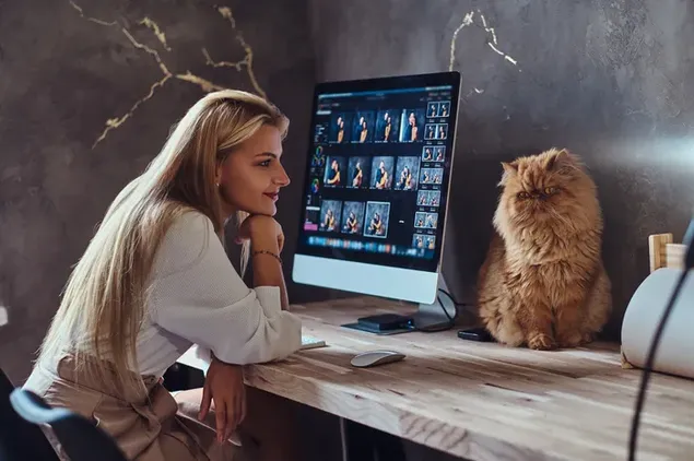 Coiled cat on wooden table and blonde model looking at computer 4K wallpaper
