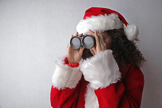 Chica rizada en traje de Santa Claus con binoculares