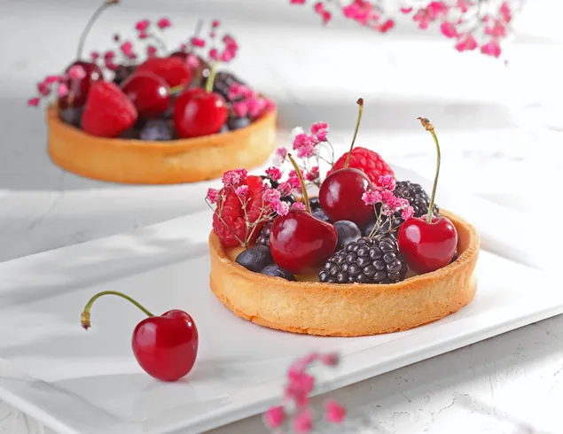 De pie sobre panqueques servidos en platos blancos con dulces frutas de verano, cerezas, moras y flores.